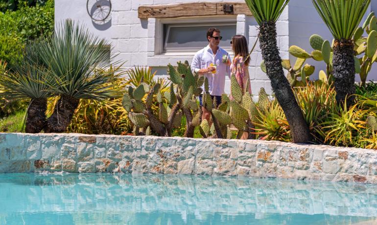 Coppia beve cocktail accanto alla piscina con piante tropicali.