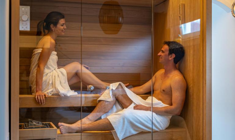 Couple heureux dans le sauna, enroulés dans des serviettes, sourires et détente.